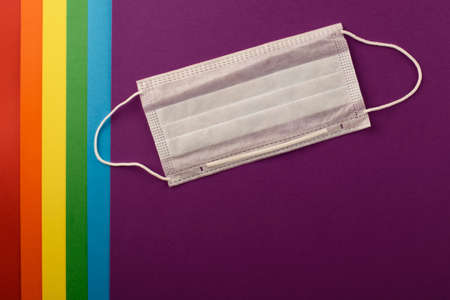 COVID-19 and Pride 2020. Individual medical mask on the background of the LGBT rainbow flag.