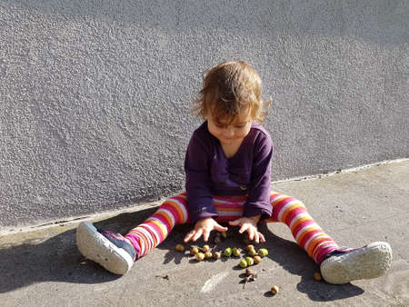 cute girl playing outdoors with wallnutsの写真素材