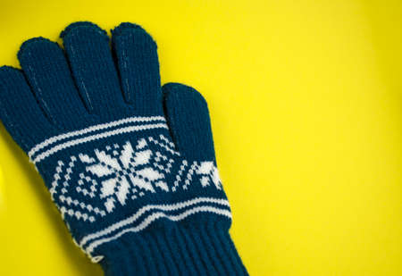 Pair of gloves isolated on the yellow background. Blue mittens close-up with copy space.