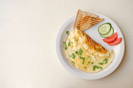 Omelet with cheese and parsley, sliced tomatoes and cucumbers on the white plate. Scrambled eggs,...