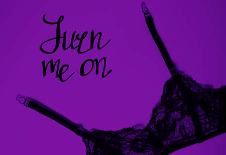 Garter belt on violet background. Turn me on, handwritten lettering. Sexy lingerie for women. Erotic underwear, black delicate girdle. Passion and romantic theme. Happy Valentine's Day!の写真素材