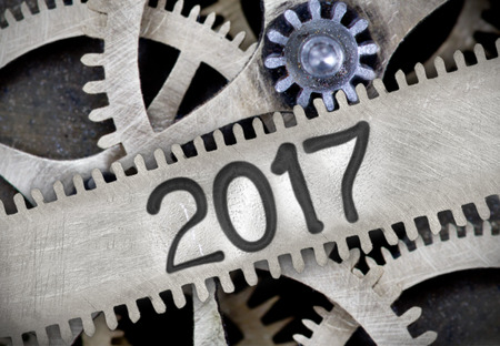 Macro photo of tooth wheel mechanism with number 2017 imprinted on clean metal surface; New Year...