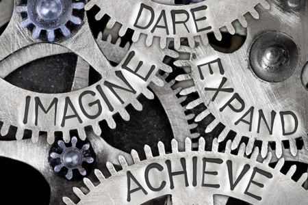 Macro photo of tooth wheel mechanism with IMAGINE, DARE, EXPAND, ACHIEVE words imprinted on metal surface; concept of IDEAの写真素材