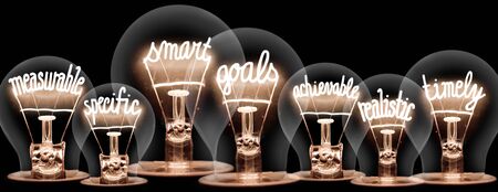 Group of light bulbs with shining fibers in a shape of Smart Goals concept related words isolated on black backgroundの写真素材