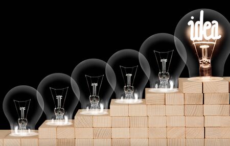Group of dimmed light bulbs and shining one of them with fiber in Idea shape isolated on black background.の写真素材