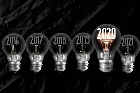 Horizontal group of shining light bulb in a shape of New Year 2020 and dimmed light bulbs with years passed isolated on black background.の写真素材