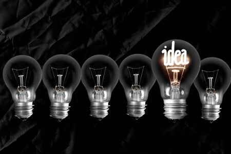 Group of dimmed light bulbs and shining one of them with fiber in Idea shape isolated on black...