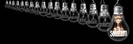 Group of shining and dimmed light bulbs with fibers in a shape of Difficulties and Solution concept words isolated on black background.の写真素材