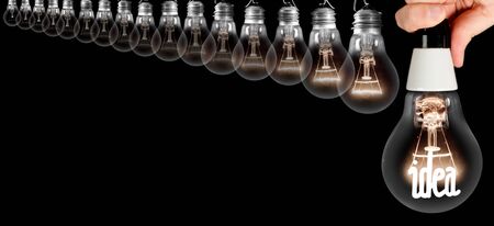 Group of light bulbs going from dark one to a shining one with fiber in Idea shape being held by a human hand isolated on black background. Concept of Thinking, Genius, Success and Creativity.の写真素材