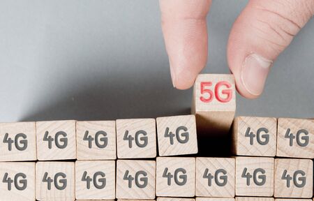 Wooden cube blocks with 5G and 4G imprinted, one of them hold by a human hand. Concept of mobile network change.の写真素材