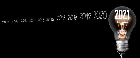 Shining light bulb with fiber in a shape of New Year 2021 and and white chalk written old years isolated on black background.の写真素材