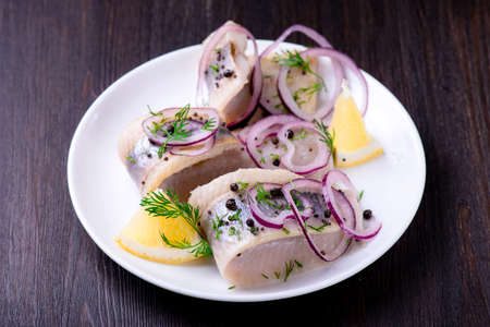 Herring with pepper, herbs, salt and lemon on white ceramic plate on black backgroundの写真素材