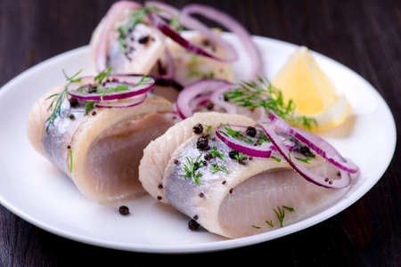 Herring with pepper, herbs, salt and lemon on white ceramic plate on black backgroundの写真素材