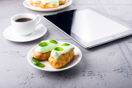 Mint eclairs on a plate, cup of coffee and digital tablet