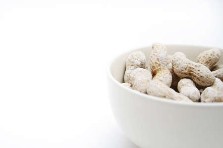 half bowl with salted peanuts on white surface to be used as backgroundの写真素材