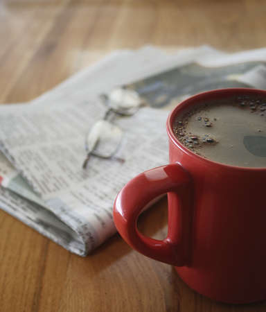 a cup of coffee, a newspaper and a pair of glasses, on a wooden tableの写真素材