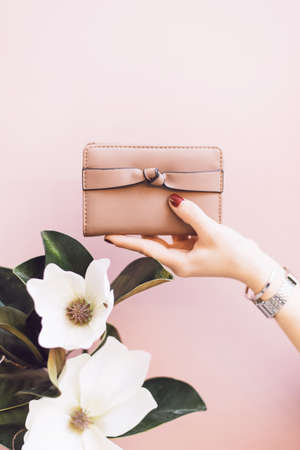Womens stylish wallet in the hands of a girl with a red manicure on a pink pastel background. A flower in the hand of a girl. The concept of style and fashion. Purse in hand.の写真素材