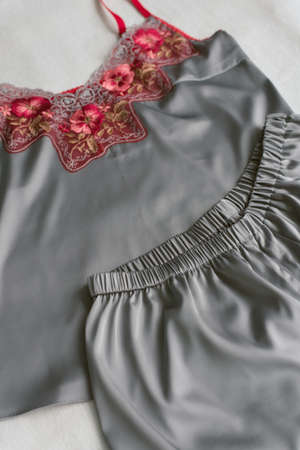 homemade silk pajamas lying on the bed without anyone. gray pajamas with red lace on a beige...