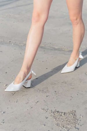 White shoes on the girl's feet. The legs in the shoes are close-up. A girl in fashionable shoes walks through the city. Asphalt underfootの写真素材