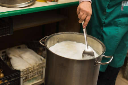 Cooking cottage cheese and cheese at home. Man creates cheese, heating milk and whey in an aluminum pan. Rustic homemade dairy productsの写真素材