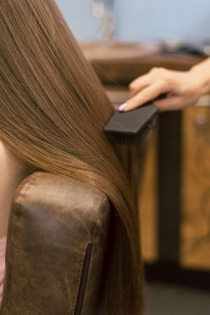 The girl in the hairdresser styled hair. Brunette in the beauty salon straighten and comb her hair....