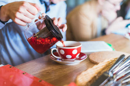 berry tea is poured into a red mug. red tea with berries is poured into a glass with white peas and...