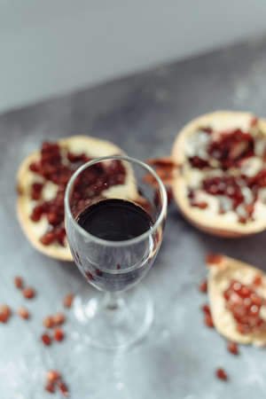 A wine glass with red wine stands on a gray grunge background next to grenades. Fruits and pomegranate wine on a concrete background.の写真素材