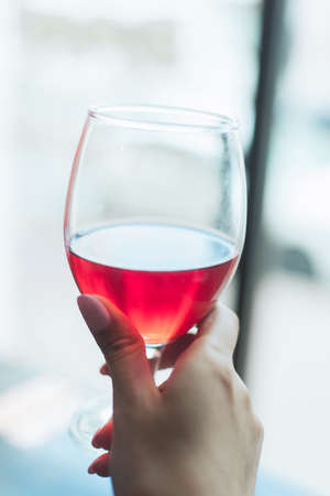 A girl with a gentle nude manicure holding a glass of cherry frothy beer. The hand of a girl holding a glass of wine.の写真素材