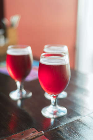 Three glasses with red wine on a wooden table. Glasses of cherry beer are on the table. A group of...