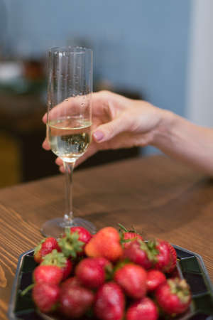 girl holding a glass of expensive sparkling champagne. Basket with large red strawberries.の写真素材