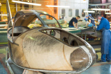 people in blue robes build a plane in the factory. Workers in overalls working on the details of the...