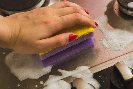 Violet - yellow sponge with a metal gas stove. Cleaning the dirt with a sponge with foam. Cleaning conceptの写真素材