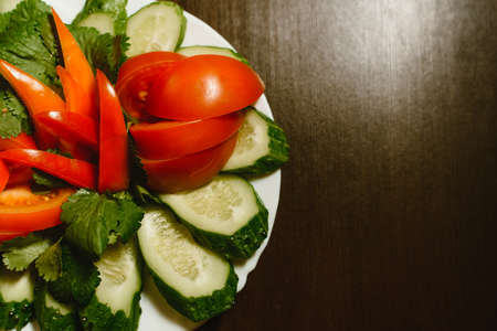 sliced tomatoes and cucumbers on a dark wooden background. Sliced vegetables on a plate. Proper...