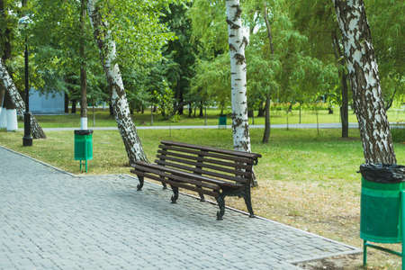 Wooden empty bench in the green park. trashcan in the park. Bench with garbage cans in a green park. The problem of garbage collection and environmental problemsの写真素材