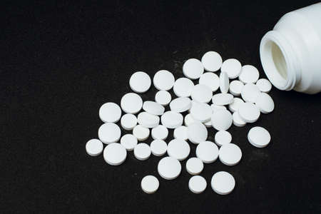 A large number of white tablets scattered from the container on a black background. concept of...