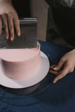 Confectioner aligns the cream with a spatula. The master of cakes lines the cream on a beige wedding cakeの写真素材