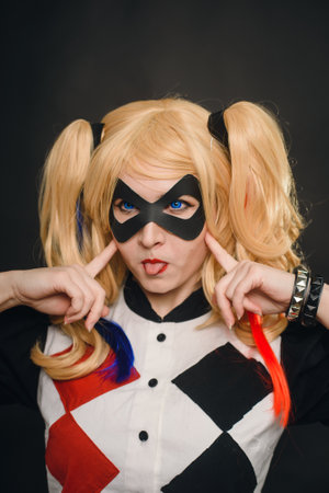 Samara Russia - 01.22.19: A girl in a suit and wig on a black background is smiling and showing tongue. Girl cosplay Harley Quinn character and having fun in the studio on Halloweenのeditorial素材