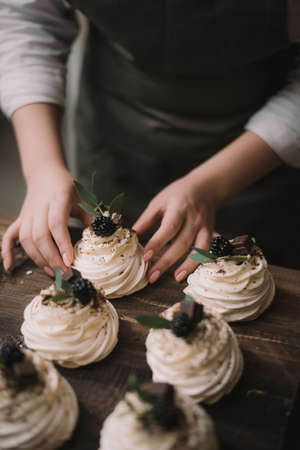 Confectioner creates a wedding dessert. Girl collects sweet dessert from meringue, chocolate and berriesの写真素材