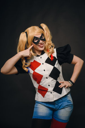A girl in a suit and wig on a black background is smiling and showing tongue. Girl cosplay Harley Quinn character and having fun in the studio on Halloween.のeditorial素材