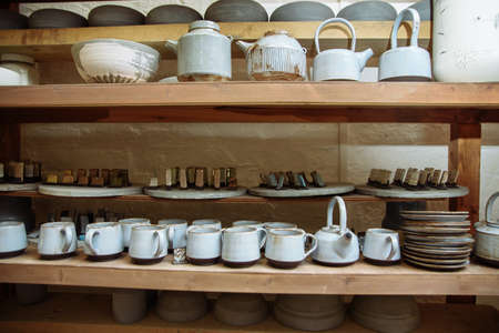 Handmade ceramic pottery in a potter's workshop. Clay plates, mugs and teapots on the shelves in the workshop studio.の写真素材