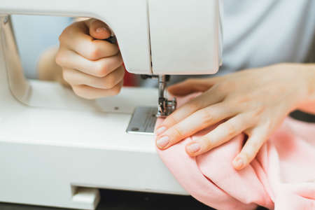 Seamstress works on a sewing machine. The girl sews and holds a pink cloth.の写真素材