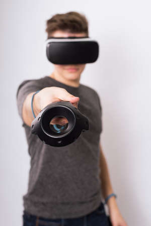 A young man holds controllers for a viar game. A teenager plays with virtual reality glasses and...
