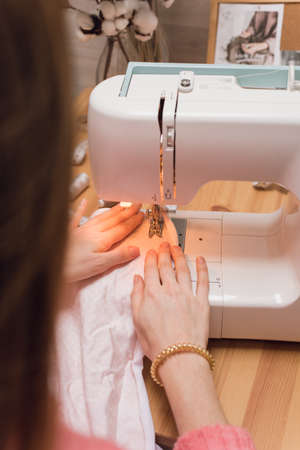 Seamstress works on a sewing machine. The girl sews and holds a pink cloth.の写真素材
