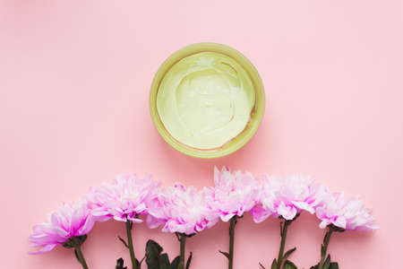 Green aloe gel in a jar on a pink pastel background next to a chrysanthemum flowers. The concept of skin hydration, skin care, natural ingredients and anti-aging. Sunburn protection, wound healing.の写真素材