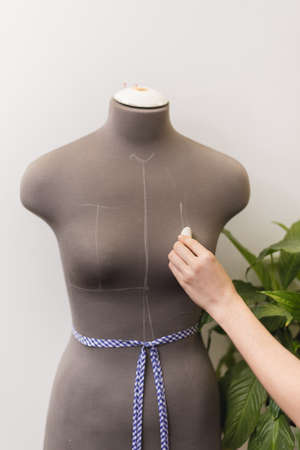 Seamstress takes measurements with chalk on a mannequin in the office. Girl idle pattern in a sewing workshop.の写真素材