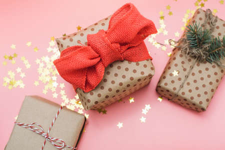 Craft gifts with red bow on pink pastel background with gold confetti. The view from the top, flat...
