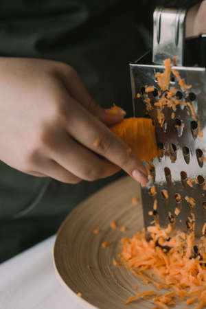 Cook the carrots rubbed on a grater into a bowl. Girl grates carrots on a grater. Out of focus, blurred.の写真素材