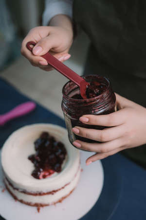 Cook puts jam with berries on the cake with cream. The pastry chef puts the jam and decorate the...