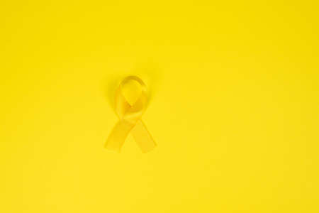 Yellow gold ribbon on a yellow background. Children cancer concept. Awareness month. Childhood Cancer Day February, 15.の写真素材