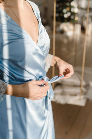 A girl in a silk robe meets morning. Woman unties the ties of a blue robe. Girl in silk underwear.の写真素材